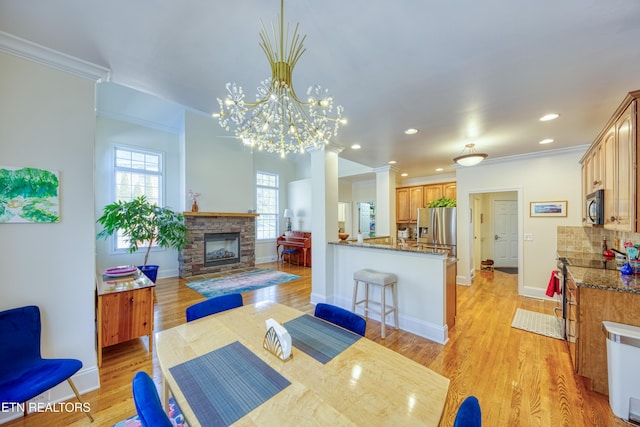 dining room featuring ornamental molding, a fireplace, and light hardwood / wood-style floors