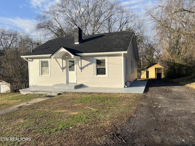 bungalow-style home featuring a front lawn, a patio area, and a storage shed