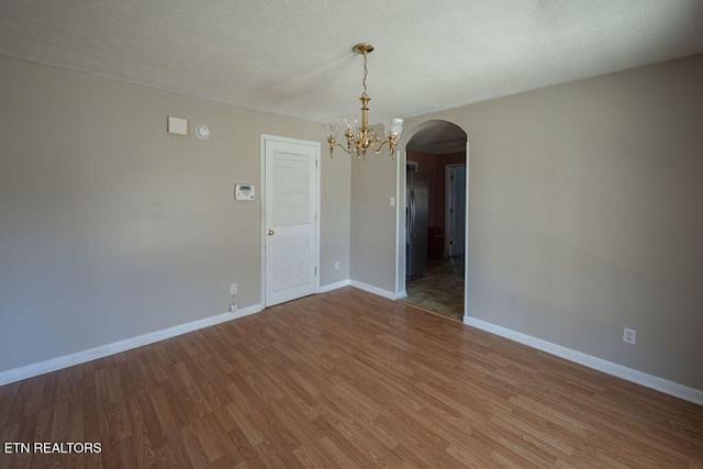 spare room featuring an inviting chandelier, hardwood / wood-style floors, and a textured ceiling