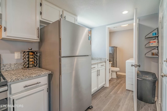 kitchen featuring light stone counters, light hardwood / wood-style flooring, stainless steel refrigerator, and white cabinets