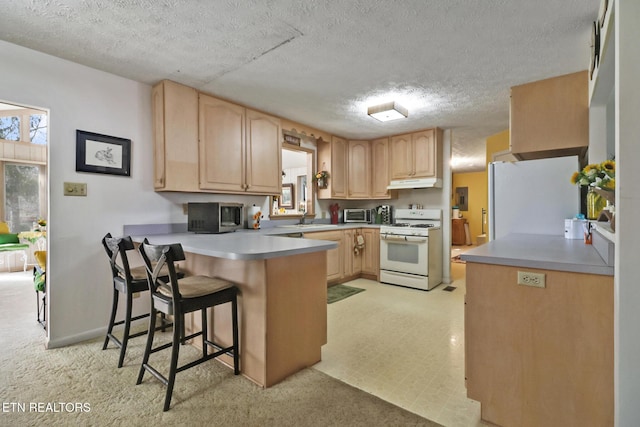 kitchen with light brown cabinetry, a kitchen breakfast bar, fridge, white range with gas stovetop, and kitchen peninsula