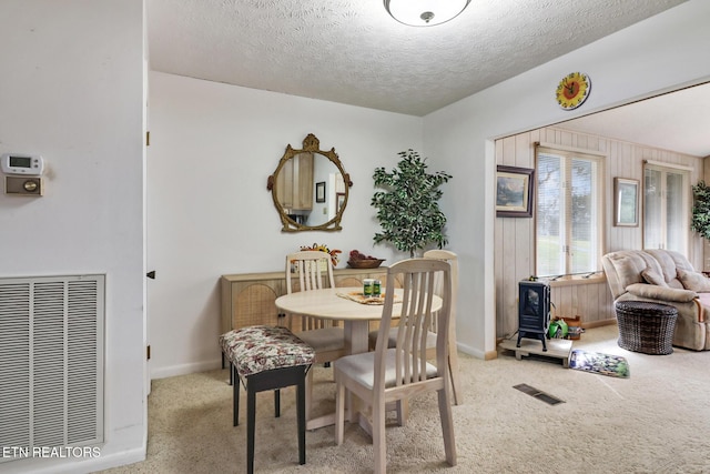 carpeted dining room featuring a textured ceiling and wood walls