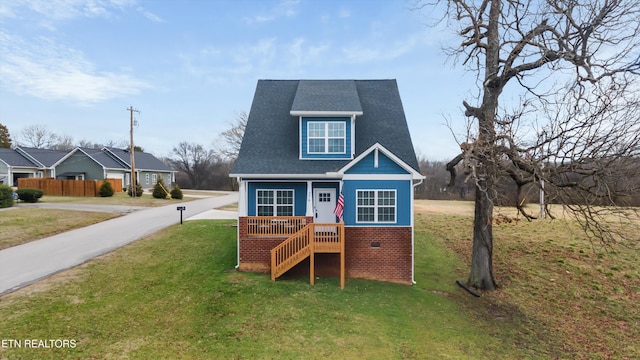 view of front facade with covered porch, a front lawn, roof with shingles, and brick siding