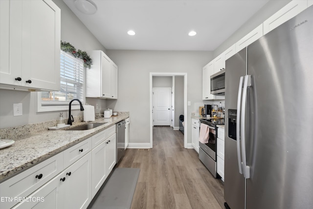 kitchen with light stone counters, appliances with stainless steel finishes, white cabinets, a sink, and baseboards