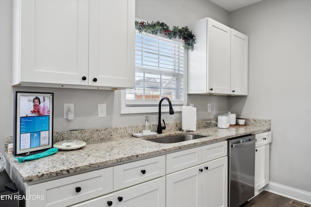 kitchen featuring white cabinets, a sink, stainless steel dishwasher, and light stone countertops