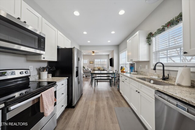 kitchen with light stone countertops, appliances with stainless steel finishes, white cabinets, and a sink