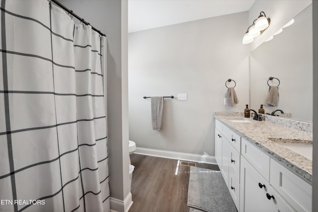 bathroom featuring wood finished floors, a sink, baseboards, and double vanity