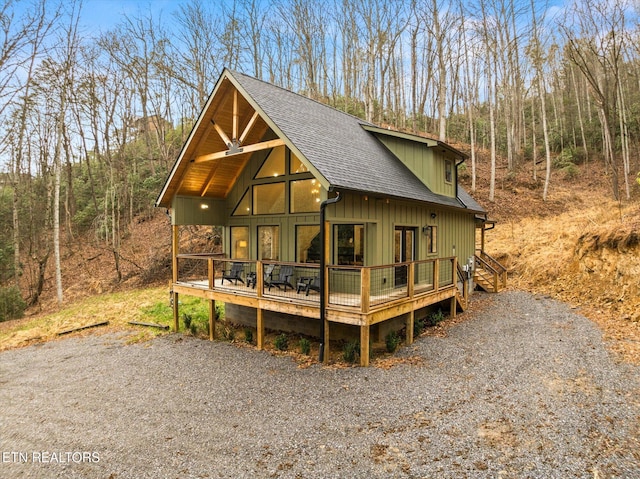 rustic home featuring a shingled roof, driveway, board and batten siding, and a forest view