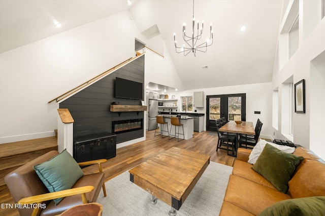 living area with light wood-type flooring, high vaulted ceiling, a glass covered fireplace, and french doors