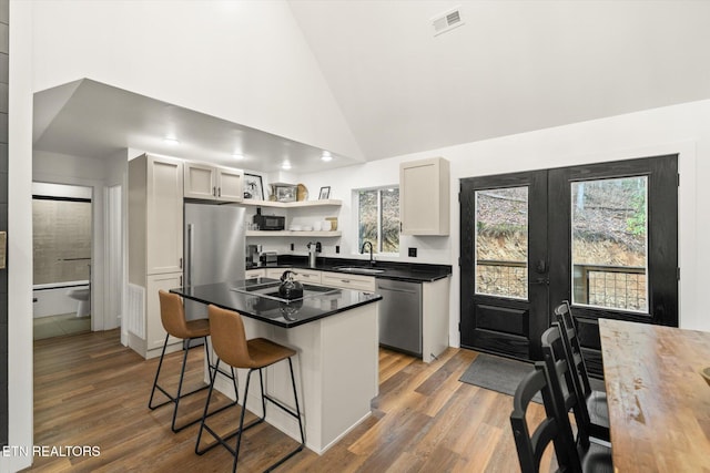 kitchen featuring dark countertops, a breakfast bar area, stainless steel appliances, open shelves, and a sink