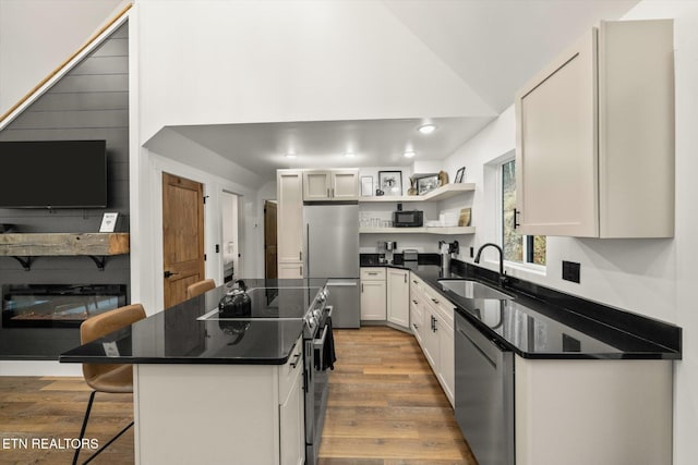 kitchen with open shelves, appliances with stainless steel finishes, a sink, wood finished floors, and a kitchen bar