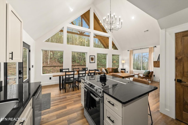 kitchen with a breakfast bar area, wood finished floors, white cabinets, stainless steel electric range, and dark countertops