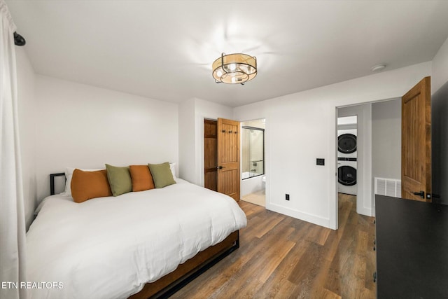 bedroom featuring stacked washer and dryer, visible vents, baseboards, connected bathroom, and dark wood-style flooring