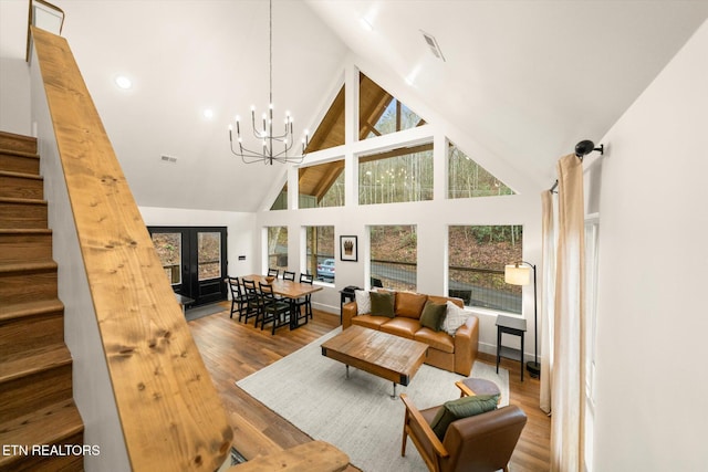 living room featuring high vaulted ceiling, wood finished floors, an inviting chandelier, and stairs