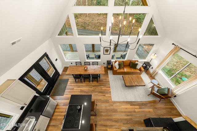 living area with baseboards, a high ceiling, wood finished floors, and an inviting chandelier