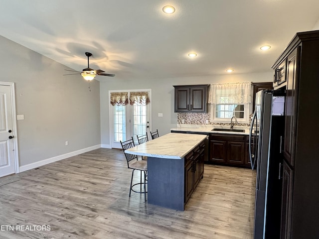 kitchen featuring sink, a breakfast bar, a center island, light hardwood / wood-style floors, and black fridge