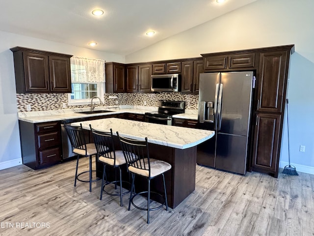 kitchen with lofted ceiling, sink, a kitchen breakfast bar, a center island, and stainless steel appliances