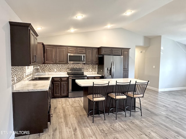 kitchen with sink, vaulted ceiling, light hardwood / wood-style flooring, appliances with stainless steel finishes, and a kitchen island