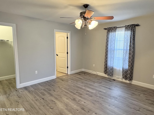 unfurnished bedroom featuring a spacious closet, light hardwood / wood-style flooring, a closet, and ceiling fan