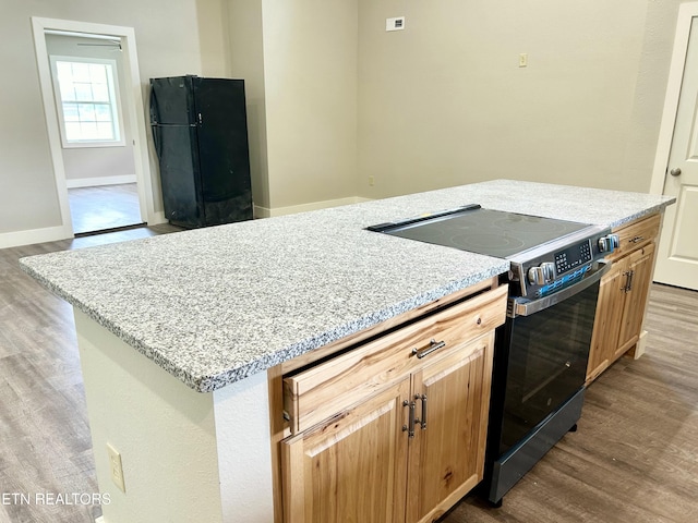 kitchen with black fridge, light stone counters, stainless steel electric range oven, light wood-type flooring, and a kitchen island