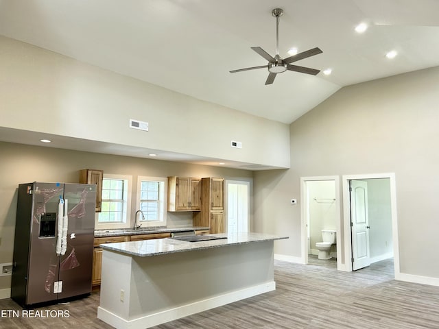 kitchen featuring sink, a kitchen island, light stone countertops, and stainless steel refrigerator with ice dispenser