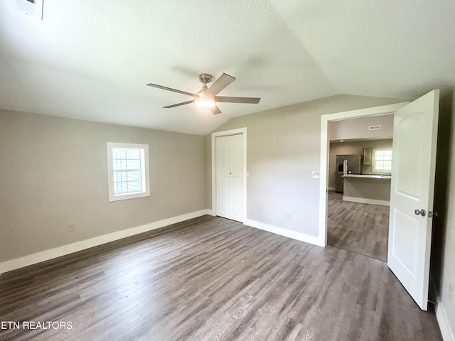 unfurnished bedroom with multiple windows, lofted ceiling, dark hardwood / wood-style floors, and a closet