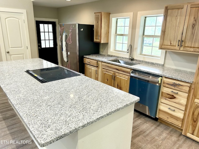 kitchen featuring appliances with stainless steel finishes, sink, a center island, light stone counters, and light hardwood / wood-style floors