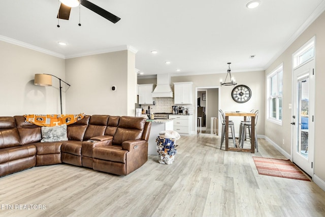 living room featuring ceiling fan with notable chandelier, ornamental molding, and light wood-type flooring