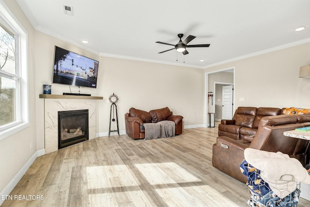 living room with crown molding, ceiling fan, a premium fireplace, and light hardwood / wood-style floors