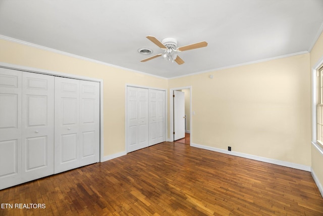 unfurnished bedroom featuring ceiling fan, ornamental molding, wood-type flooring, and two closets