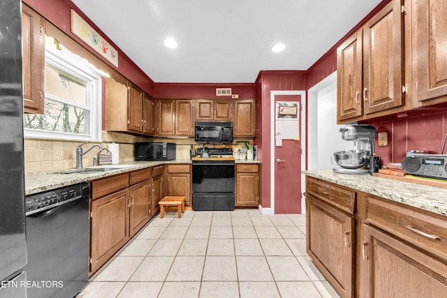 kitchen featuring light tile patterned flooring, sink, light stone counters, black appliances, and backsplash