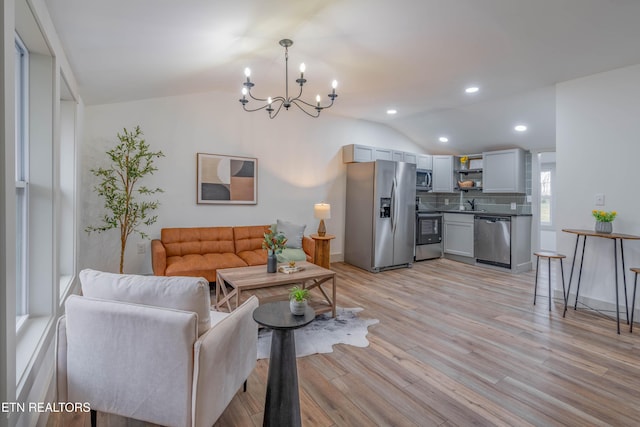 living room with lofted ceiling, sink, a notable chandelier, and light wood-type flooring