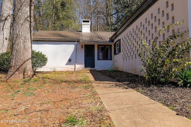 view of exterior entry featuring stucco siding, a chimney, and metal roof