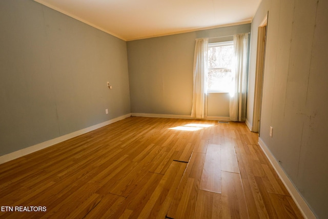 empty room with light wood-style flooring, crown molding, and baseboards