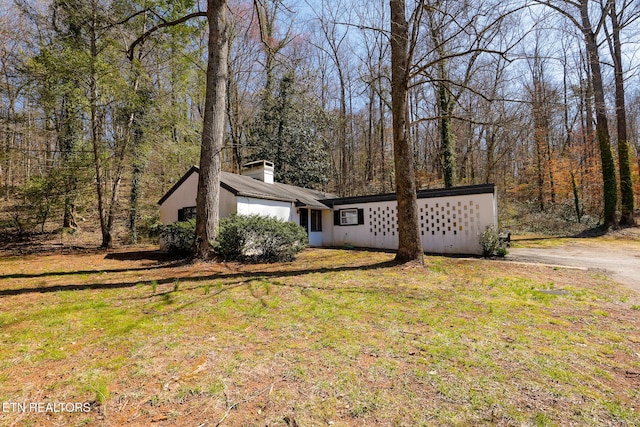 view of front facade with a chimney, a wooded view, and a front lawn