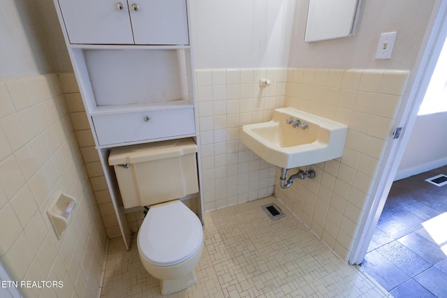 half bath with visible vents, a sink, tile patterned flooring, tile walls, and toilet