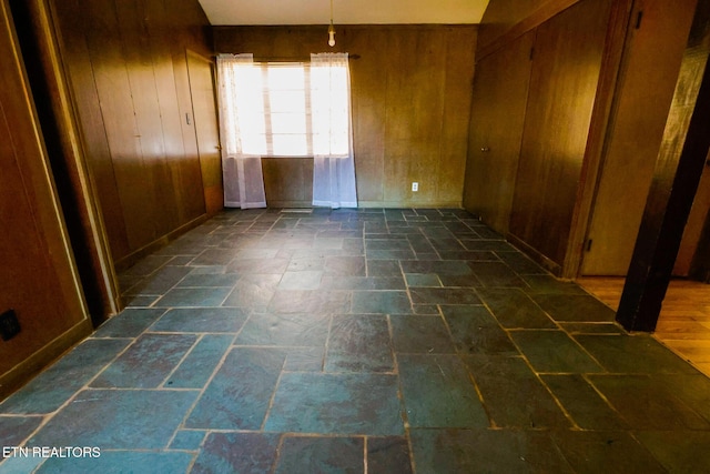 spare room featuring stone tile flooring and wood walls