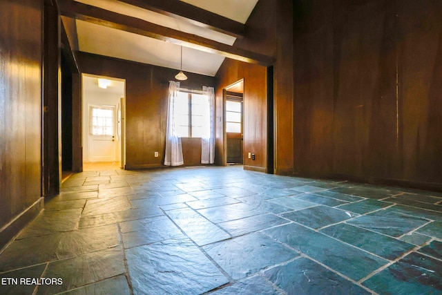 empty room featuring stone tile flooring, wood walls, and vaulted ceiling with beams