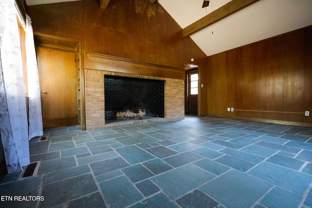 unfurnished living room featuring visible vents, a brick fireplace, beamed ceiling, wood walls, and stone tile flooring