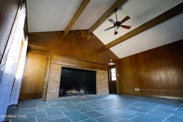 unfurnished living room with beam ceiling, high vaulted ceiling, stone tile flooring, wooden walls, and a fireplace