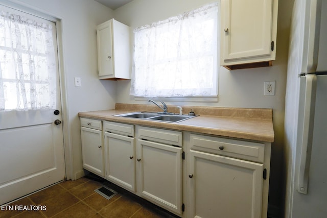 kitchen with visible vents, freestanding refrigerator, a sink, light countertops, and white cabinetry