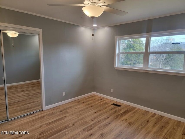 unfurnished bedroom with hardwood / wood-style flooring, crown molding, ceiling fan, and a closet