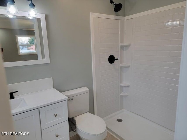 bathroom featuring a tile shower, vanity, and toilet