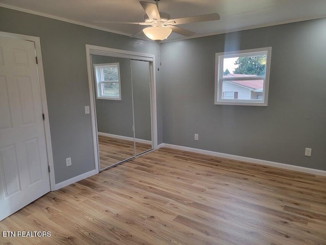 unfurnished bedroom featuring multiple windows, ornamental molding, light hardwood / wood-style floors, and a closet