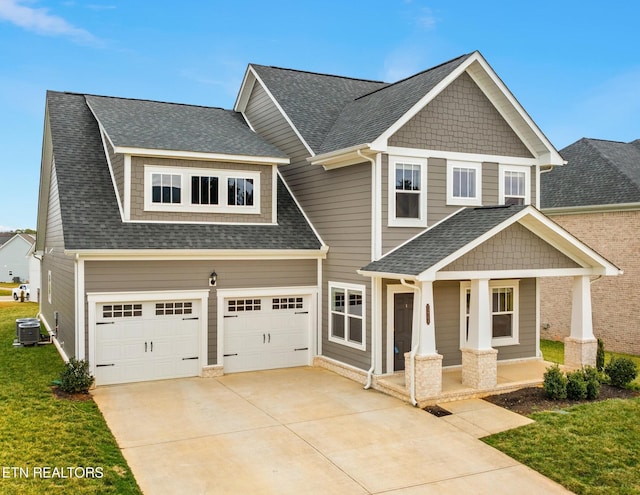 craftsman-style home featuring cooling unit, roof with shingles, covered porch, concrete driveway, and a front lawn