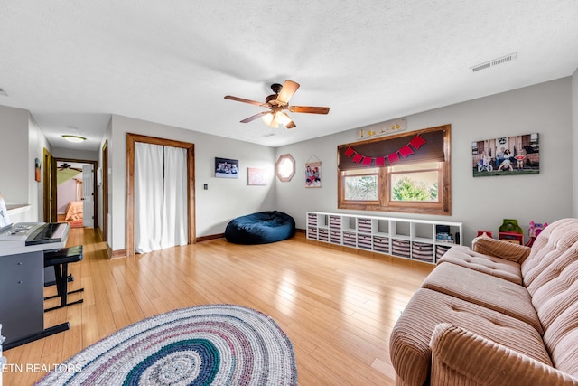 living room featuring ceiling fan, a textured ceiling, and light hardwood / wood-style floors