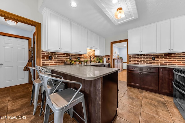 kitchen featuring a breakfast bar, dark brown cabinets, double oven range, kitchen peninsula, and backsplash