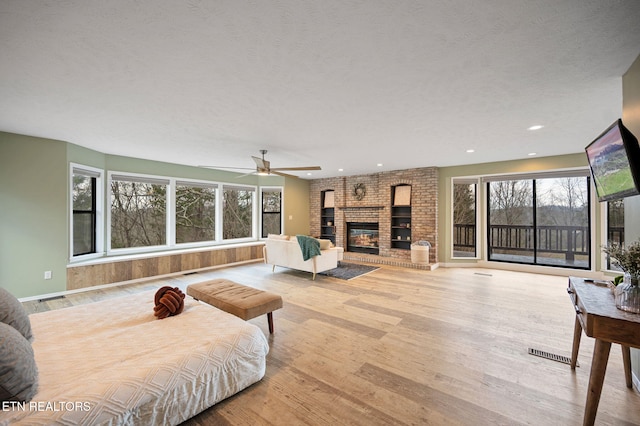 living room featuring ceiling fan, a fireplace, light hardwood / wood-style floors, and a textured ceiling