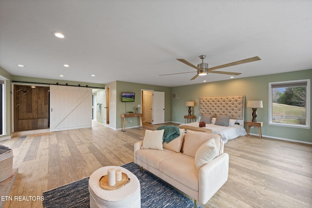 bedroom with a barn door, ceiling fan, and light hardwood / wood-style flooring