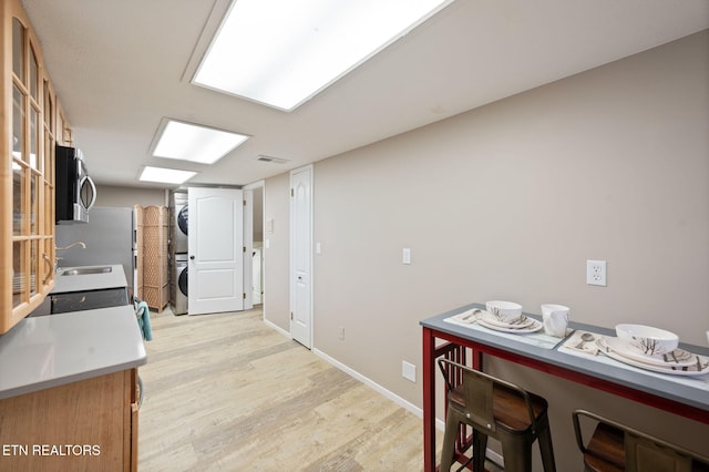 kitchen featuring sink, a breakfast bar area, stacked washer and clothes dryer, and light wood-type flooring